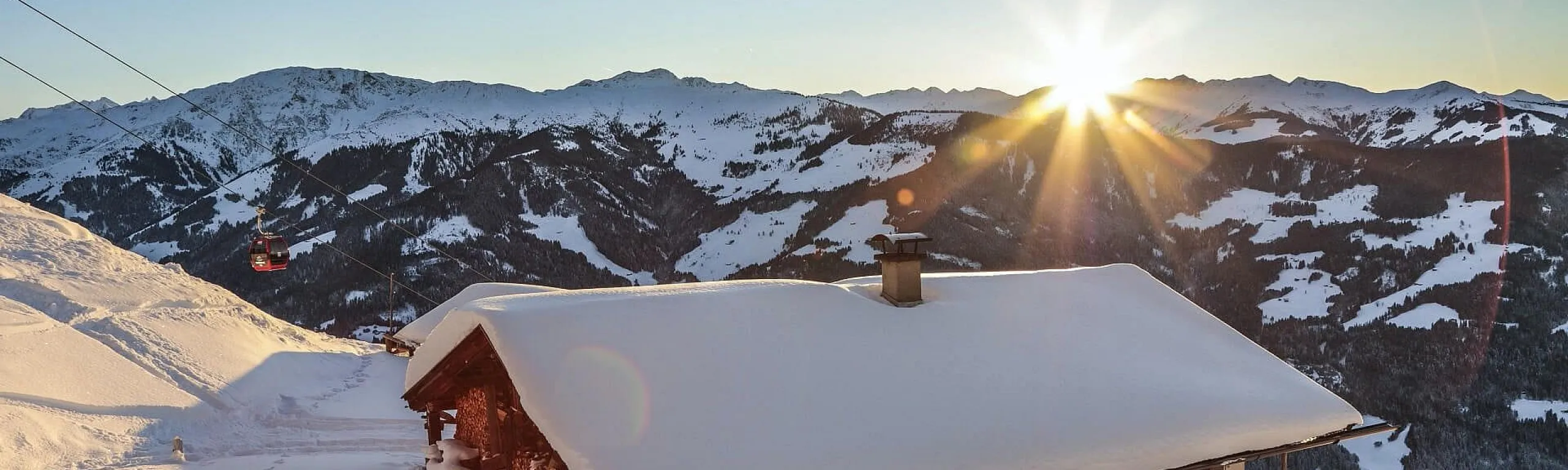 Schneebedecktes Dach mit Berglandschaft im Hintergrund und Sonnenaufgang