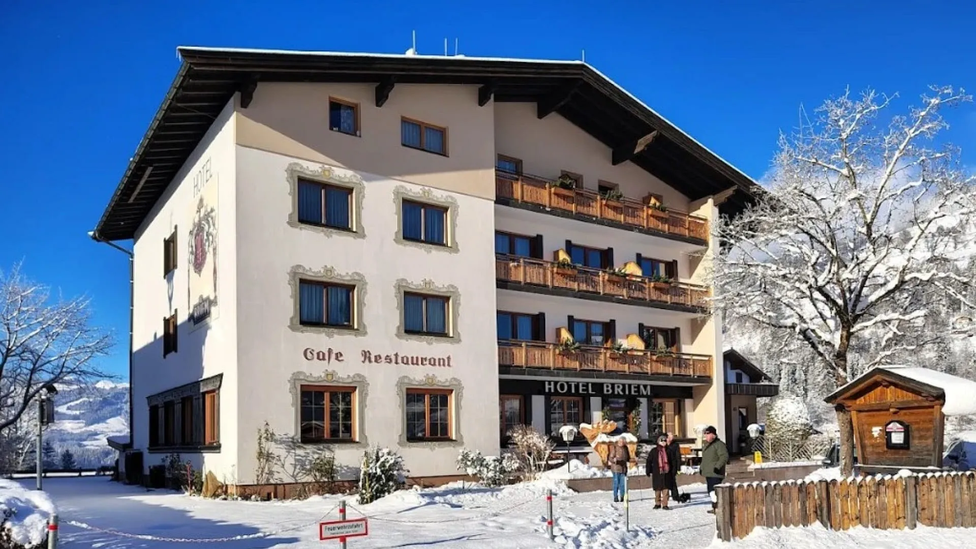 Hotel Briem im Winter, verschneite Landschaft, Personen vor dem Gebäude