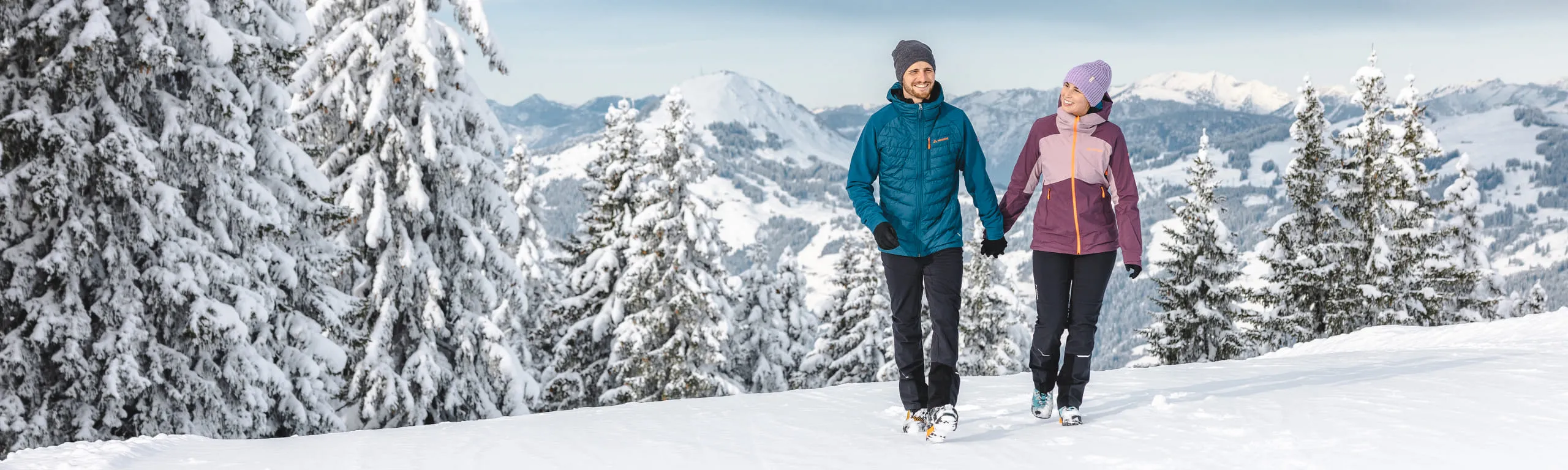 Zwei Personen wandern durch eine verschneite Winterlandschaft.